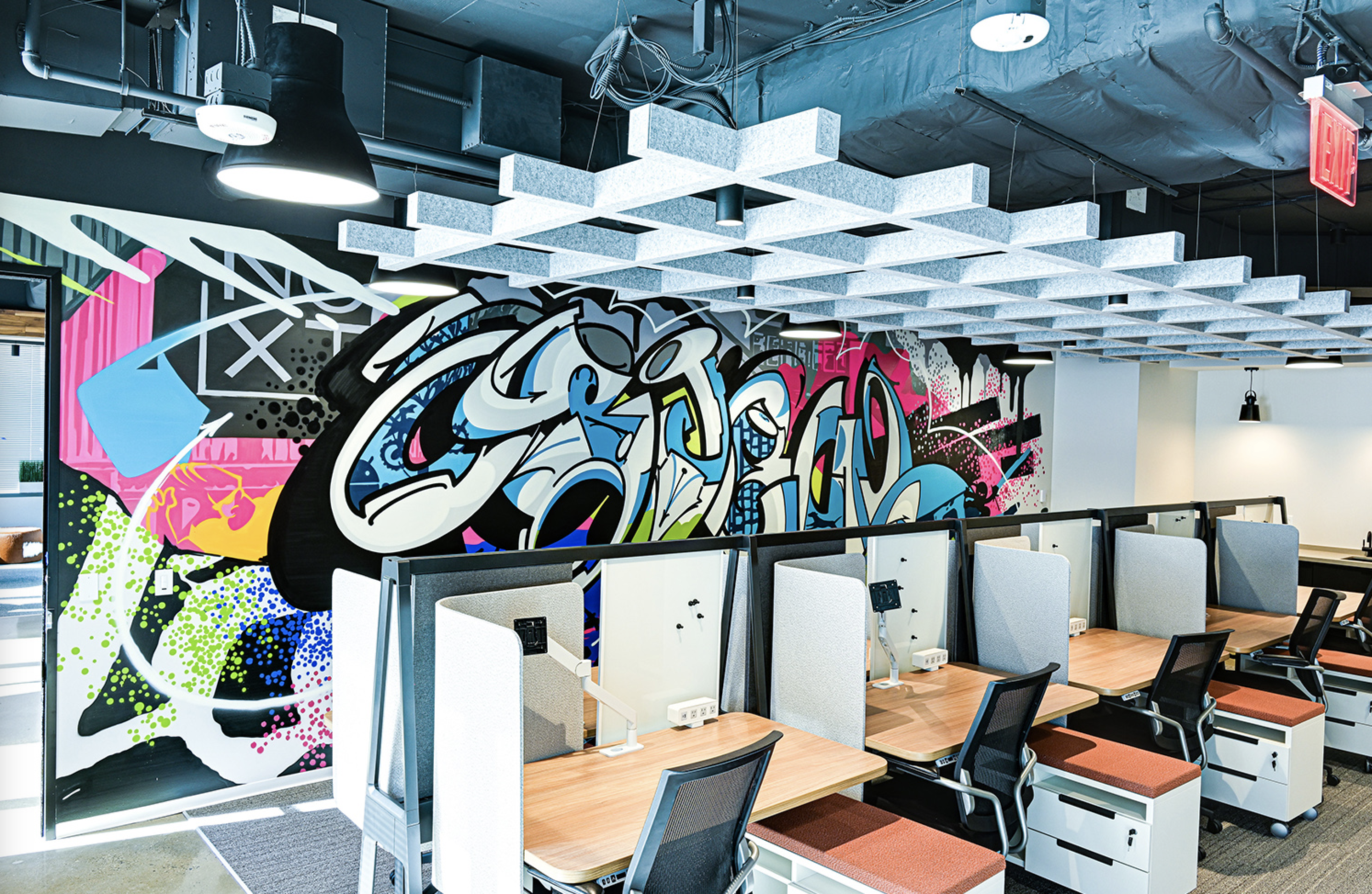 Modern office space with colorful graffiti art on the walls and acoustic panels on the ceiling.