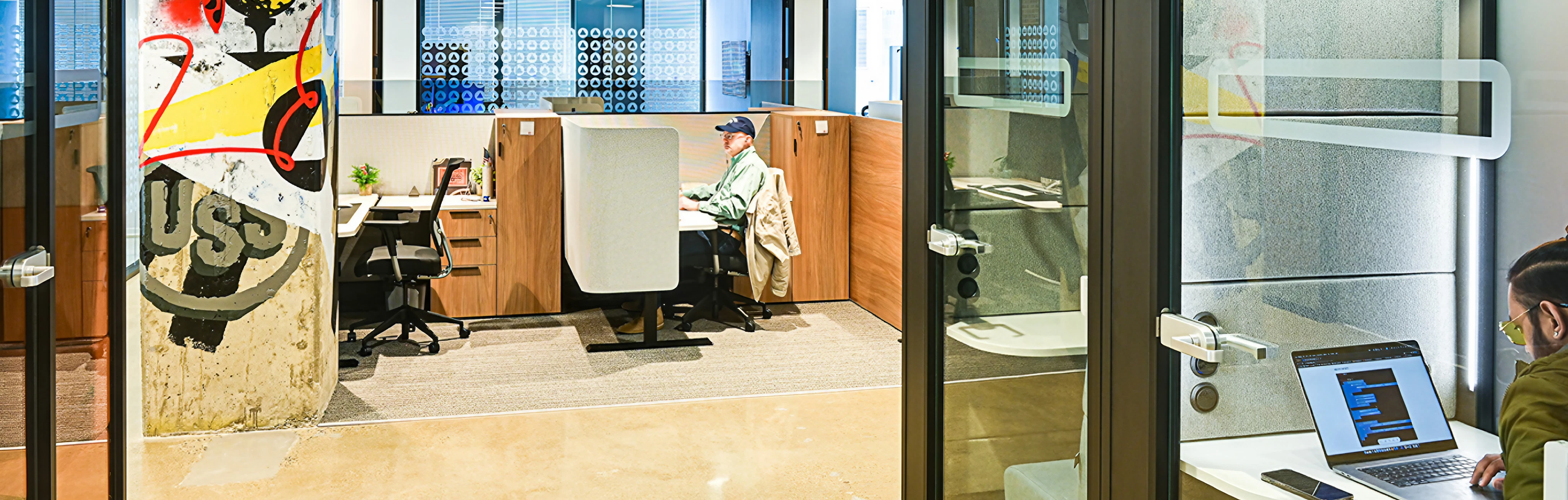 Modern office space with employees working at desks and a colorful graffiti-style pillar.