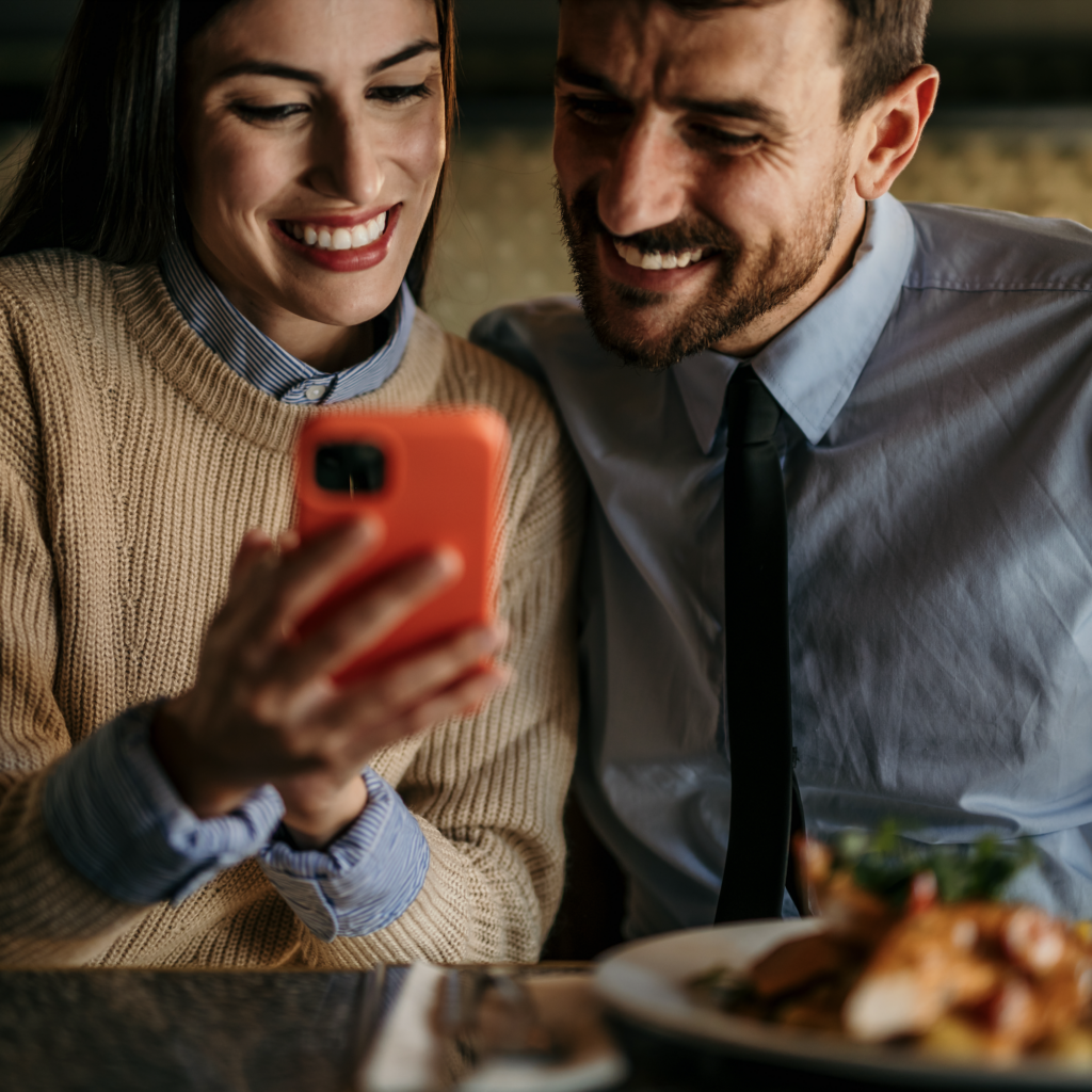 Smiling couple with a smartphone at a dining table.